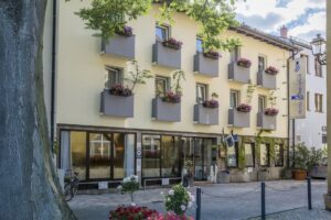 Die Außenansicht des Hotel Brunner Amberg mit hellgelber Fassade, Blumenkästen an den Balkonen und Leuchtreklame.